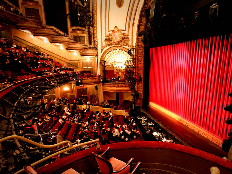 Inside a Broadway theater — the audience, ornate auditorium and red stage curtain
